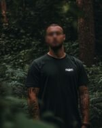 Muškarac u crnoj majici s natpisom 925 – Rex Croatorum, stoji u gustoj šumi, djelomično zamagljenog lica